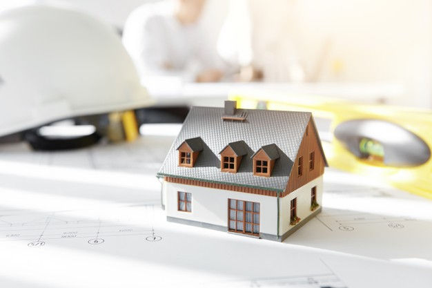 Maquette de maison posée sur des plans, à côté d’un casque de chantier